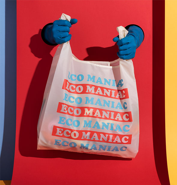 Two blue-gloved hands emerging from a colorful backdrop hold an Eco Maniac reusable shopping bag with items inside
