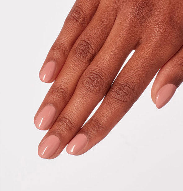 Model's hand wears a neutral, muted pink shade of nail polish