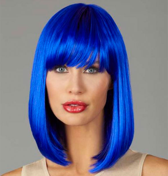 Model wearing a shoulder length, bright blue wig with bangs.