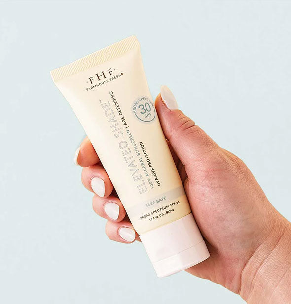 Model's hand holds a bottle of FarmHouse Fresh Elevated Shade 100% Mineral Sunscreen with an SPF of 30