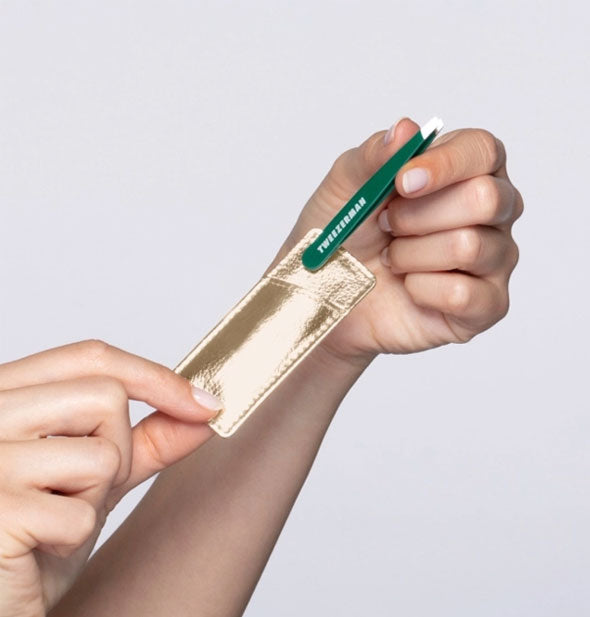 Model's hands pull a mini green Tweezerman brand tweezer from a metallic gold pocket case