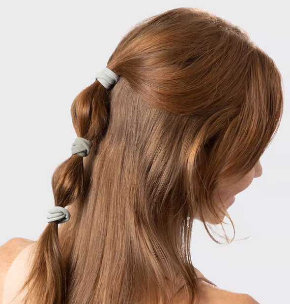 Model wears three light green hair elastics in a half-up ponytail