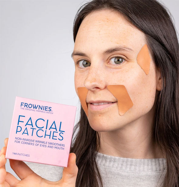 Model holding Frownies Facial Patches box demonstrates use of patches with two applied to the sides of her mouth and one near her temple