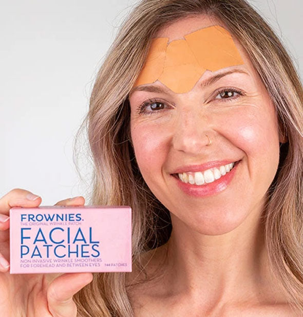 Model holding Frownies Facial Patches pack demonstrates use of product with patches shown applied on her forehead