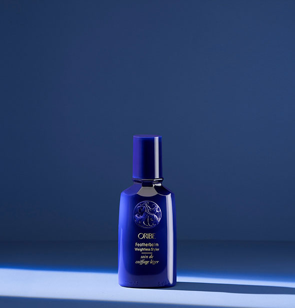 Small royal blue bottle of Oribe Featherbalm Weightless Styler on blue background