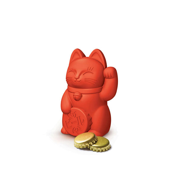 Red silicone lucky cat bottle opener alongside two gold bottle caps