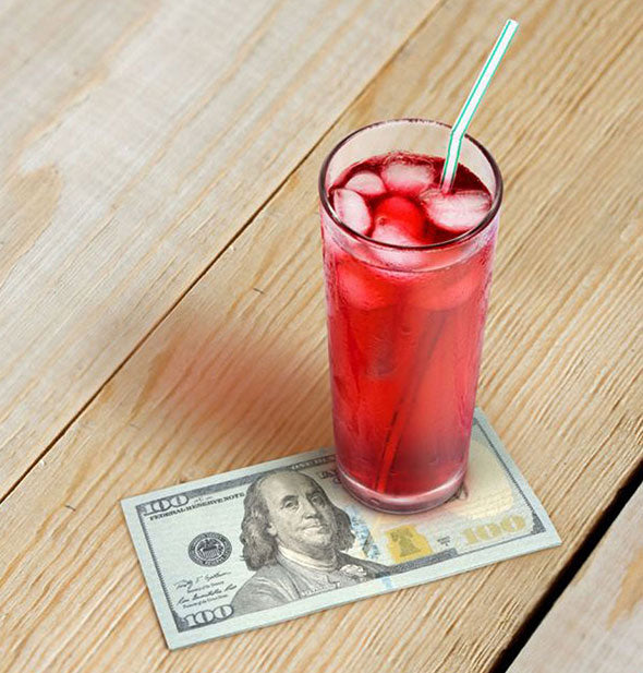 A cocktail with 100 dollar bill napkin sit on a wooden surface
