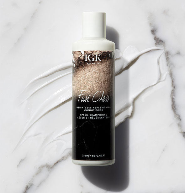 Bottle of IGK First Class Weightless Replenishing Conditioner with product sample surrounding on a marble backdrop