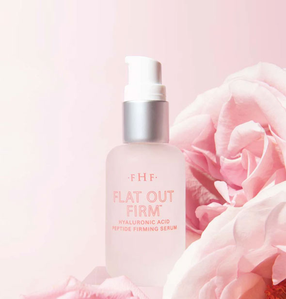 Frosted glass bottle of FHF Flat Out Firm Hyaluronic Acid Peptide Firming Serum on a pink background with pink roses