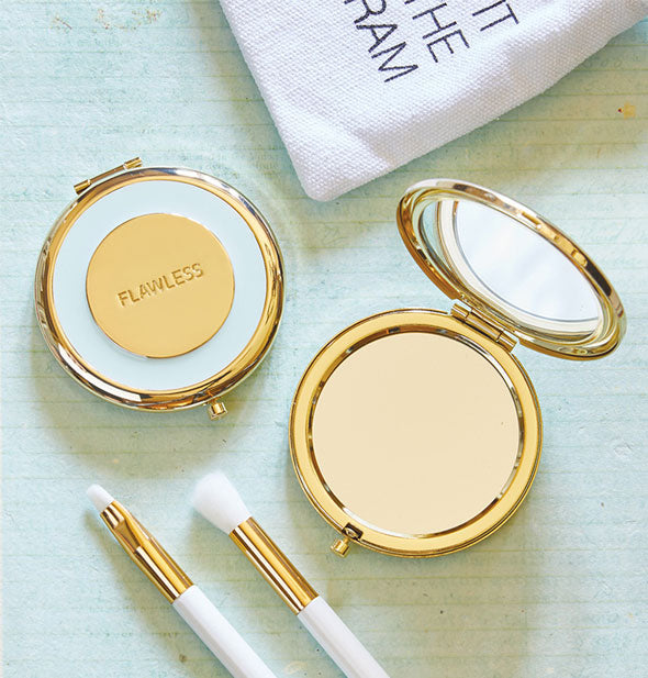 Round blue and gold Flawless compact mirror shown open and closed with makeup brushes and bag