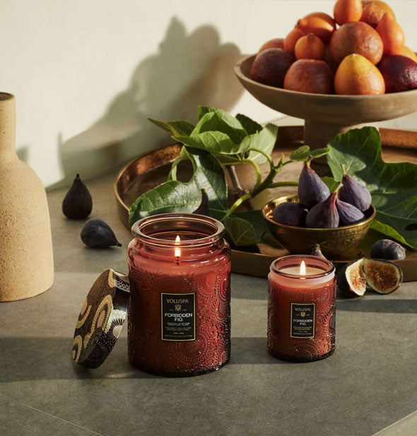 Small and large brown embossed glass candles staged with figs and pears in the background