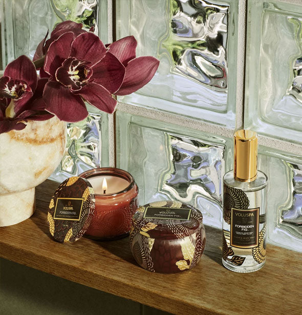Glass and metal candles staged with florals on a wooden shelf in front of glass block window