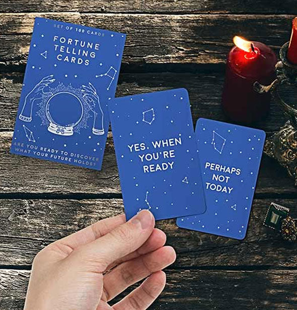 Model's hand holds a sample Fortune Telling Card against a mysterious candlelit wooden background