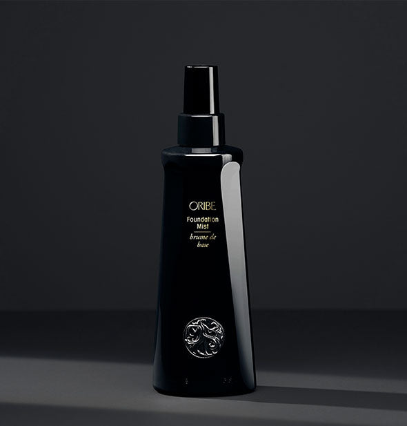 Black bottle of Oribe Foundation Mist on dark gray background