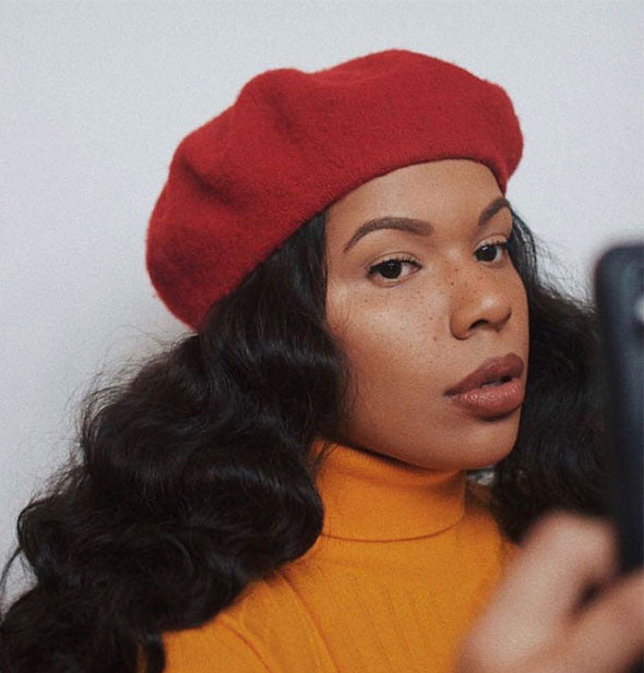 Model in red beret and yellow sweater wears Freck faux freckles cosmetic on cheeks and nose