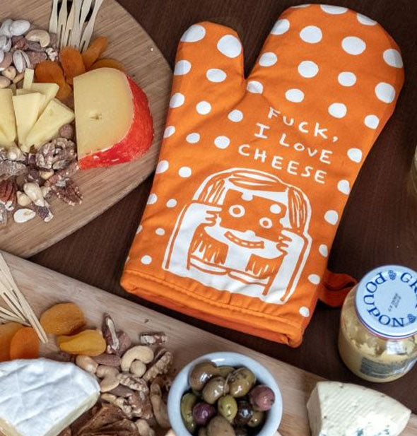 Orange and white "Fuck, I Love Cheese" polkadot oven mitt sits next to two charcuterie boards and a jar of mustard