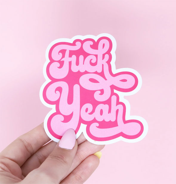 Model's hand holds a pink and white sticker that says, "Fuck Yeah" in decorative bubble script lettering