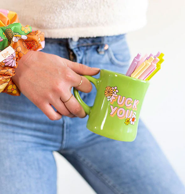 Model holds a green Fuck You mug with pens in it