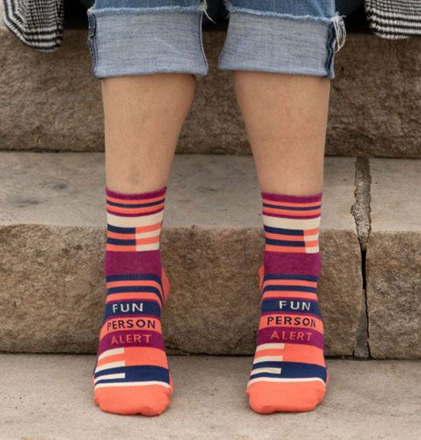 Model sitting on concrete steps wears a pair of Fun Person Alert socks