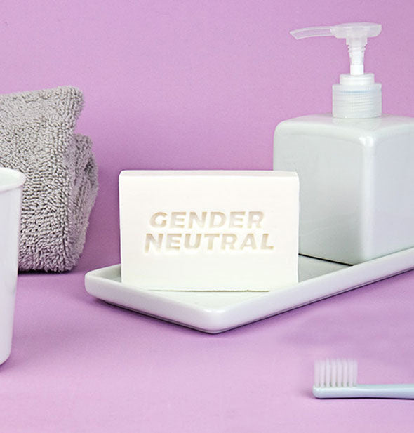 Bar of white Gender Neutral soap staged with other bath toiletries on a purple background