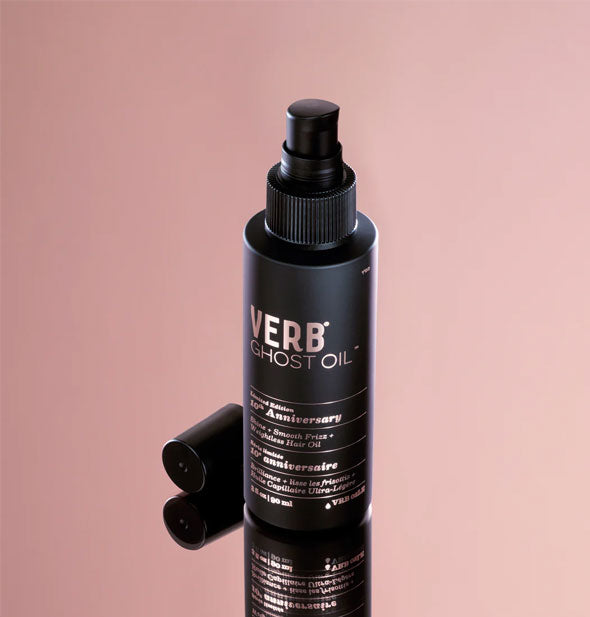 Black bottle of Verb Ghost Oil with metallic pink lettering and with cap removed rests on a mirrored surface