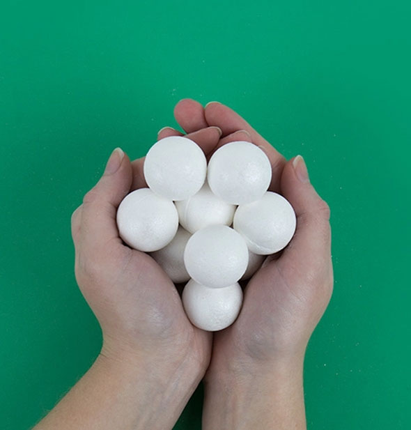 Model's hand holds a bunch of whitish-silver bath bombs against a green backdrop