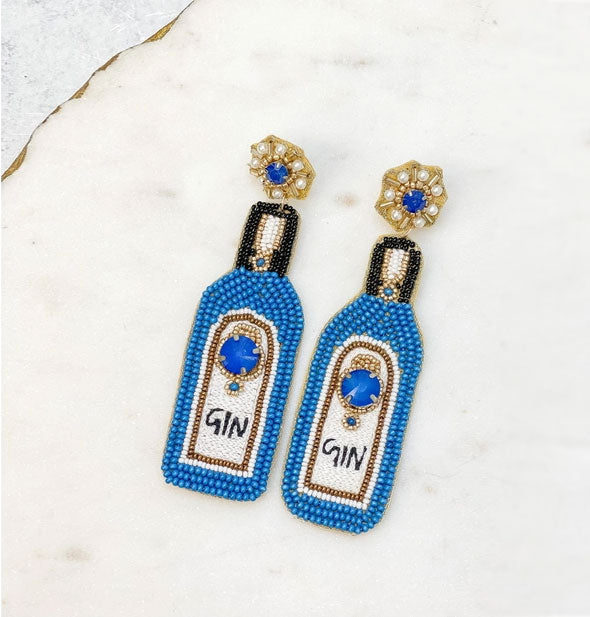 Blue, black, white, and gold beaded "Gin" dangle drop earrings on a marbled surface