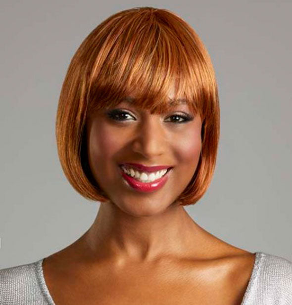 Model wearing a short, strawberry blonde wig with bangs.