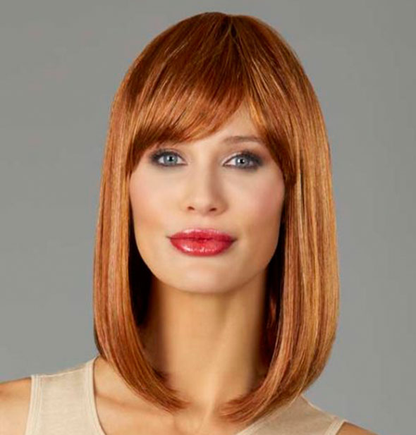 Model wearing a shoulder length, strawberry blonde wig with bangs.