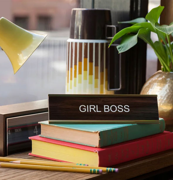 Retro-style faux wood Girl Boss desk sign is staged with books, pencils, and other office accoutrements