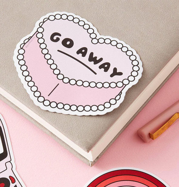 Go away heart cake sticker on a notebook cover with pen and other stickers surrounding it