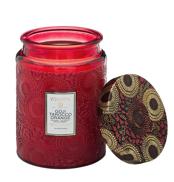Red embossed glass Goji Tarocco Orange Voluspa jar candle with red and gold metallic floral lid set to the side