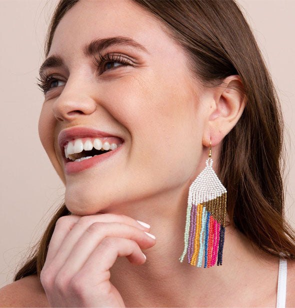 Smiling model wears a pair of white and gold beaded fringe earrings with colorful hanging strands