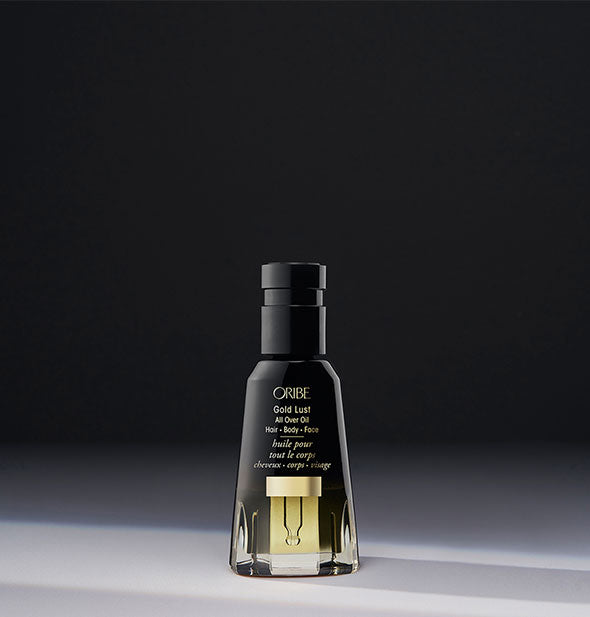 Black and gold bottle of Oribe Gold Lust All Over Oil on dark gray background