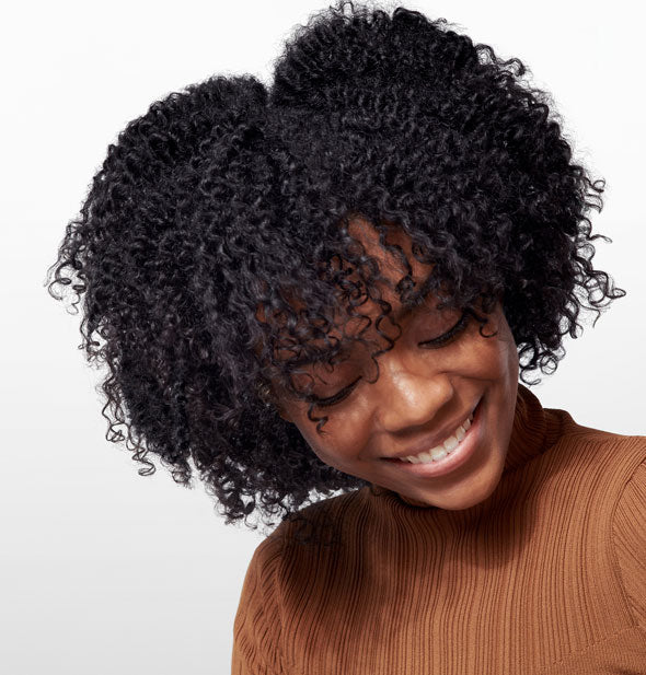 Model with very tight, textured curl pattern demonstrates the result of using Oribe Gold Lust Nourishing Hair Oil