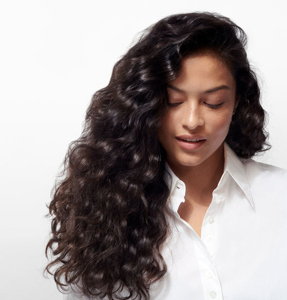 Model with long, loose curls demonstrates the result of using Oribe Gold Lust Nourishing Hair Oil