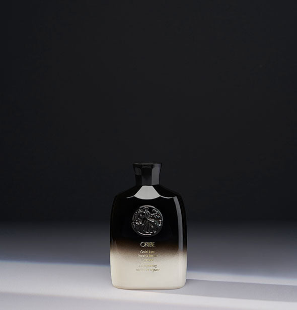 Travel size black-to-white bottle of Oribe Gold Lust Repair & Restore Shampoo on gray background
