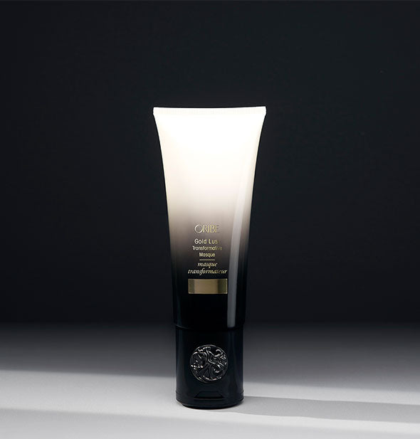 White-to-black ombre bottle of Oribe Gold Lust Transformative Masque on dark shadowy background