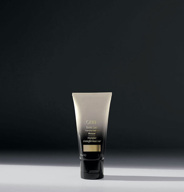 White-to-black ombre mini bottle of Oribe Gold Lust Transformative Masque on dark shadowy background