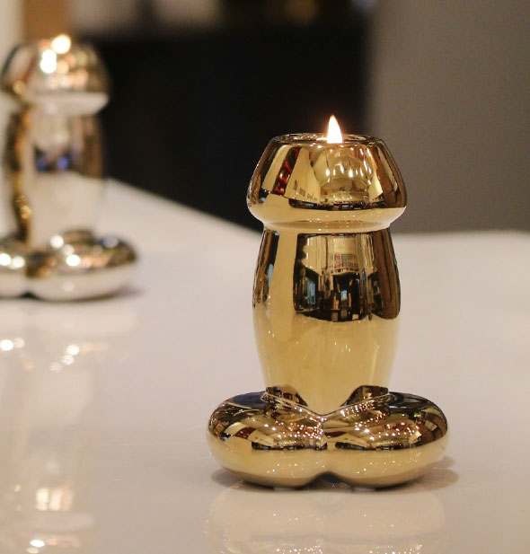 Shiny gold penis-shaped candle on a white countertop