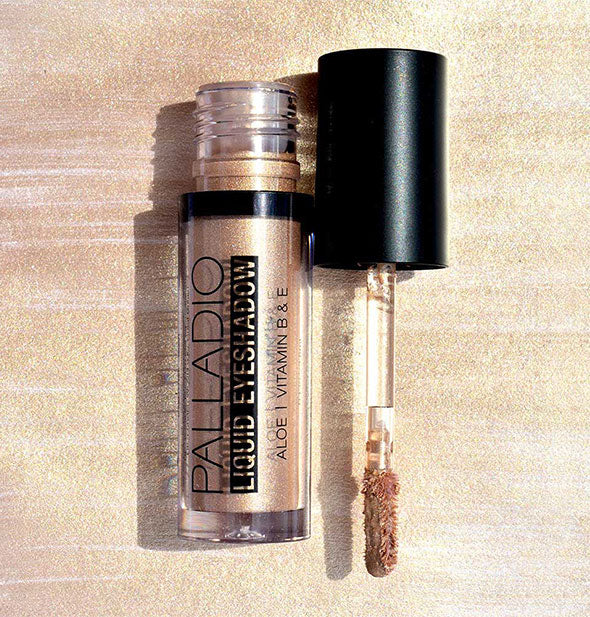 Tube of Palladio Liquid Eyeshadow with applicator wand removed against background sample color swatch in a light metallic gold shade