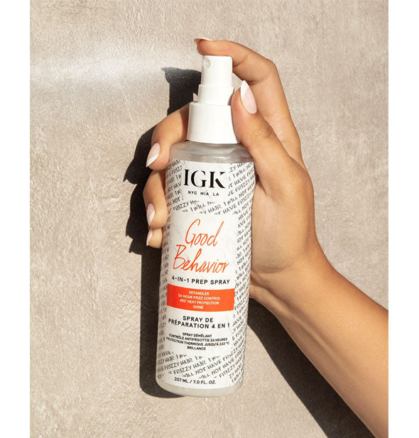 Model's hand dispenses a mist of IGK Good Behavior 4-In-1 Prep Spray from bottle