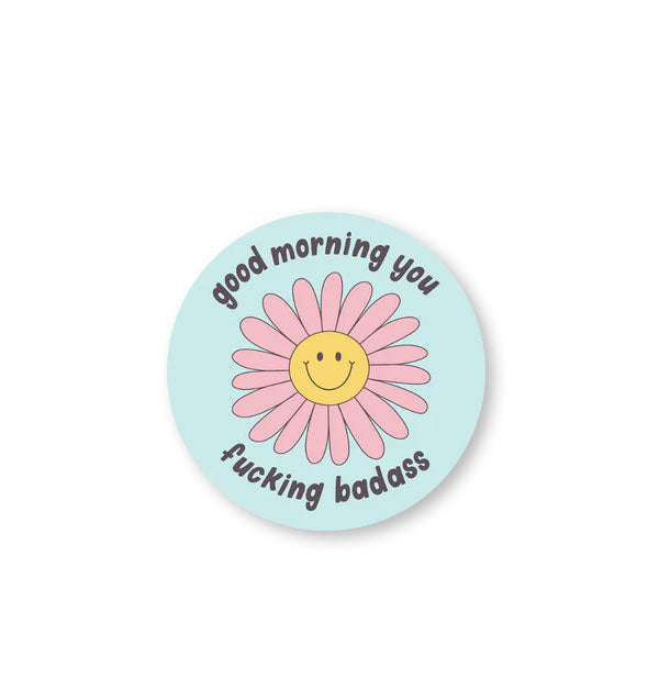 Round blue sticker with central illustration of a smiling daisy says, "Good morning you fucking badass" at top and bottom in dark lettering