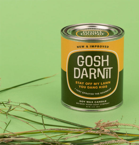 Gosh Darn It Paint Can Candle is staged with blades of grass on a green background