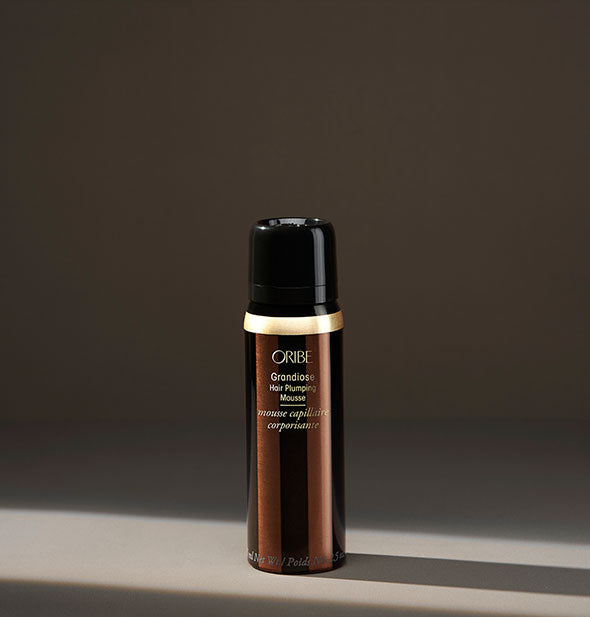 Small dark brown and gold can of Oribe Grandiose Hair Plumping Mousse on shadowy background