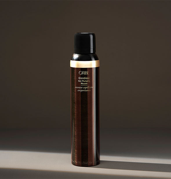 Dark brown and gold can of Oribe Grandiose Hair Plumping Mousse on shadowy background