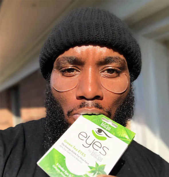 Model holding a pack of ToGoSpa Green Tea Eyes between lips wears a pair of the under-eye gel patches