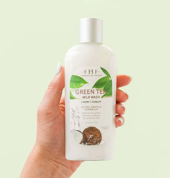Model's hand holds a 6 ounce bottle of FarmHouse Fresh Green Tea Milk Wash Cream Cleanser against a light green background