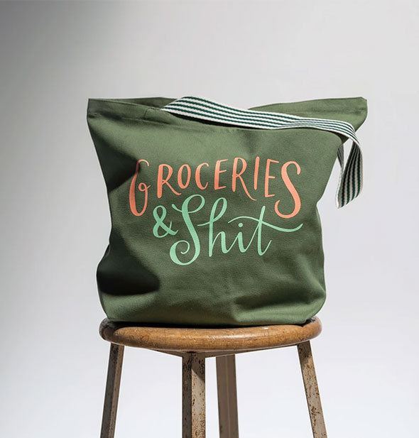 Groceries & Shit tote bag sits on a wooden stool