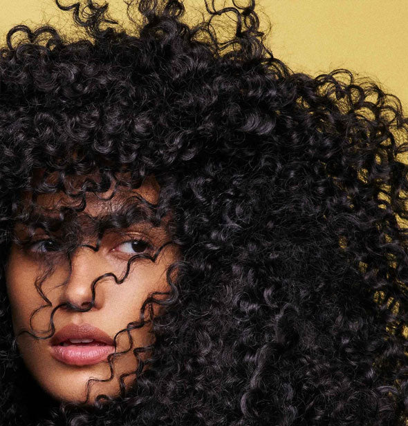 Model with very curly hair demonstrates the effects of using Oribe's Hair Alchemy products